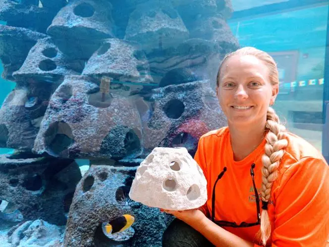 Capt. Nikki holding a memorial reef module beside a display of reef structures.